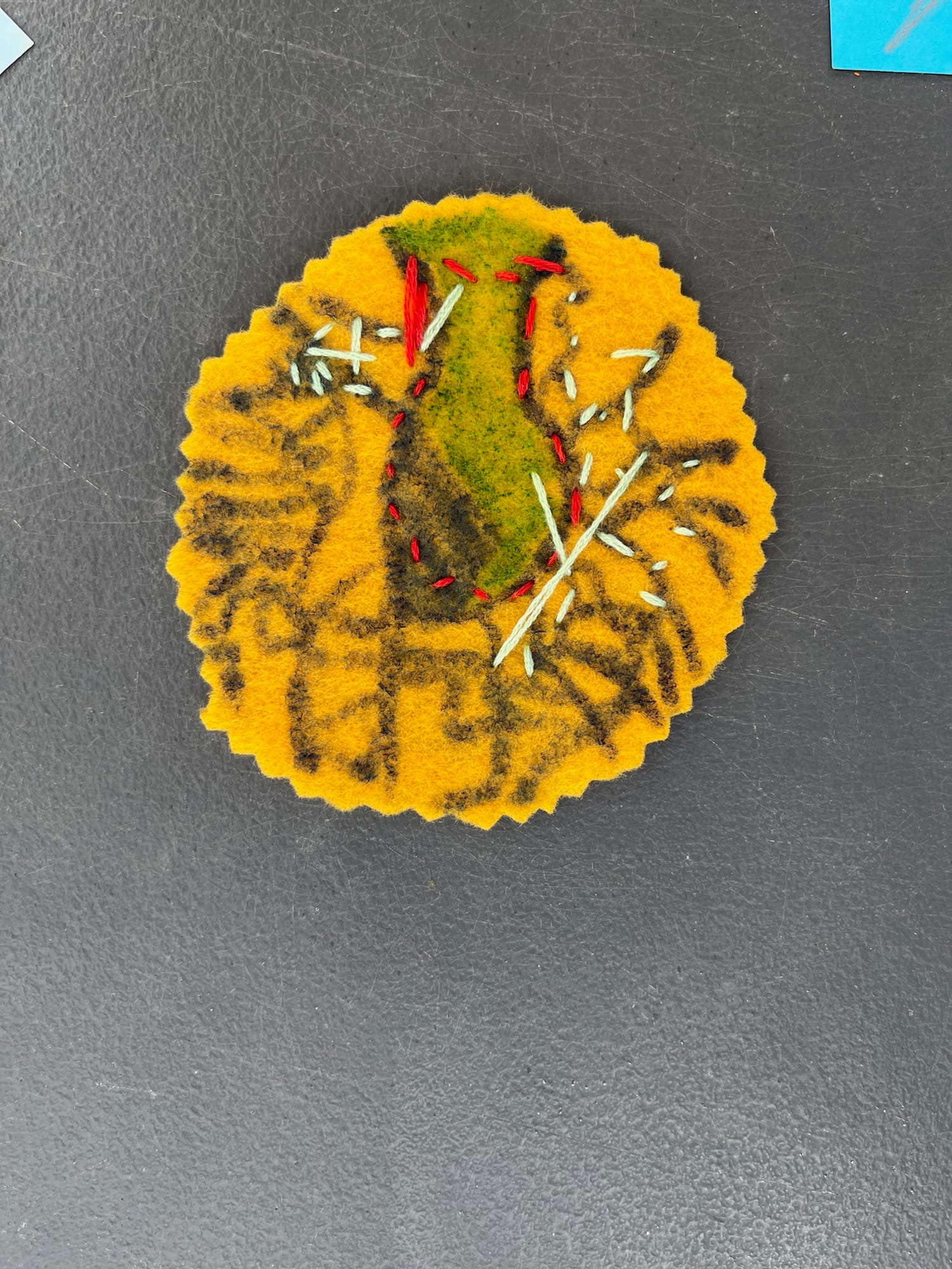 A green plant stitched onto a mustard felt circle