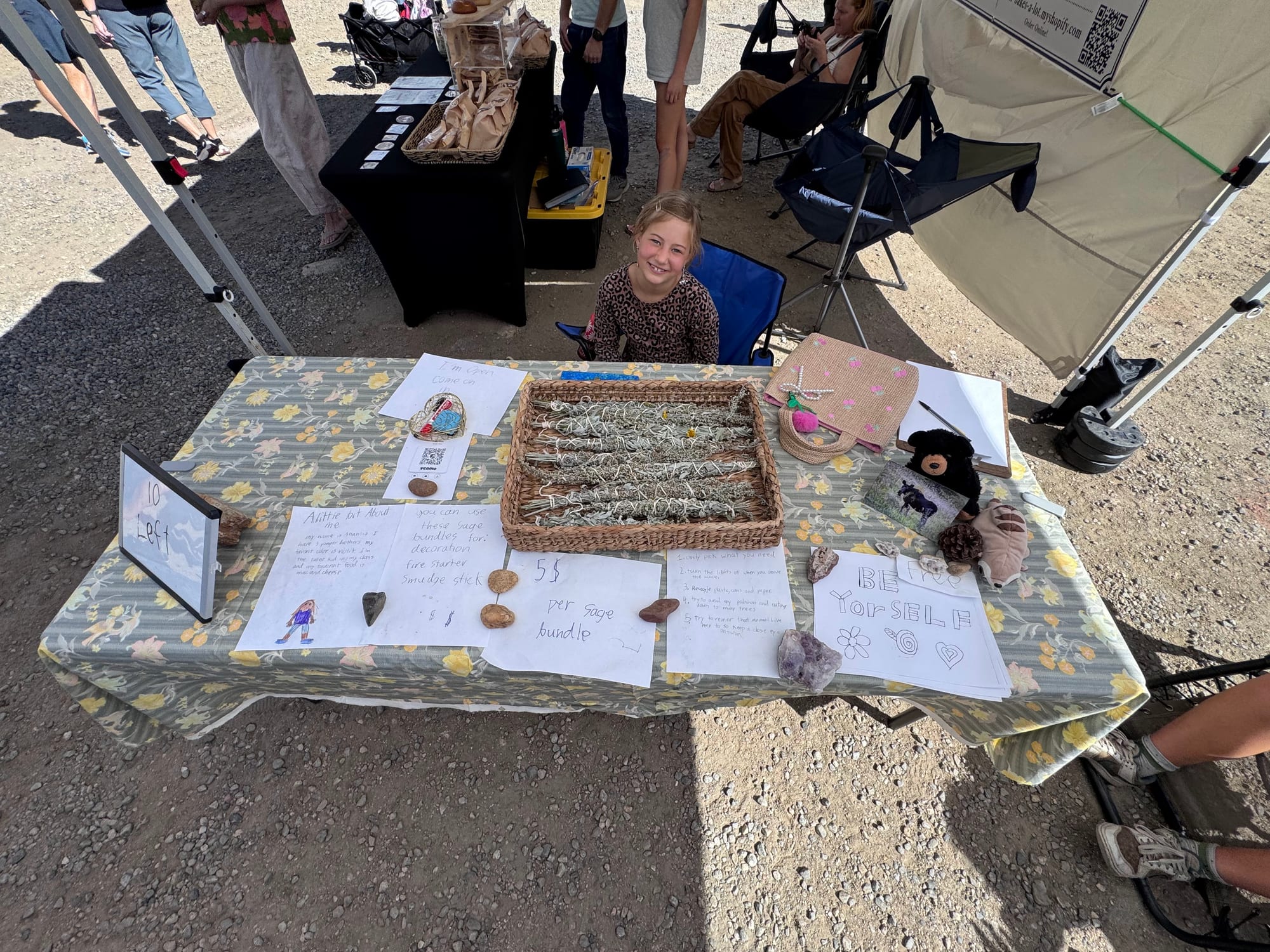 A kid vendor behind a table of hand-tied sage bundles