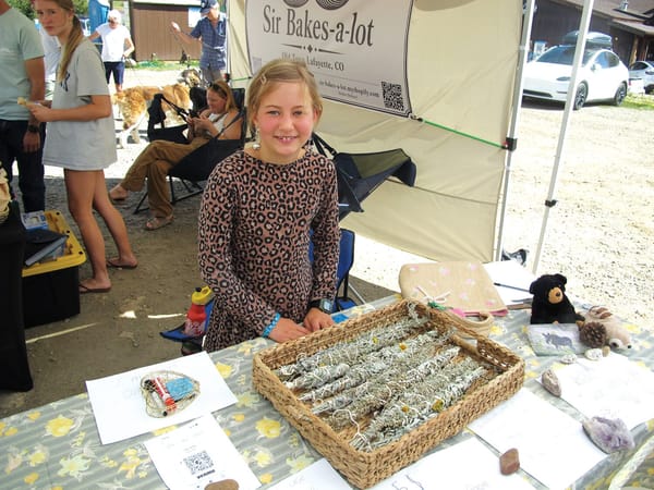 A young vendor behind a table of hand-tied sage bundles at the Kids Mini Market